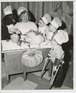 Connie Boswell dressing Thanksgiving turkey with young clients and poodle in chef's hat