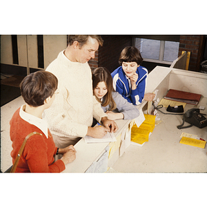Family watcheing as man fills out form at the front desk of the YMCA
