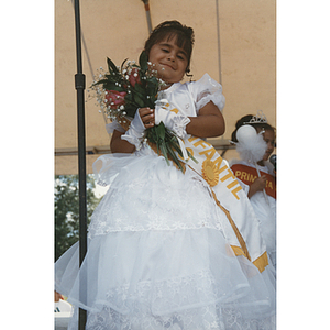 The Child Queen holds a bouquet of flowers on stage at the Festival Puertorriqueño