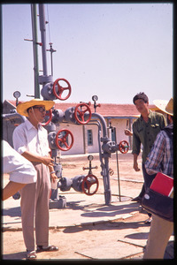 Man addressing group at oil field in front of wellhead pressure regulator