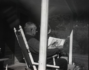 Older man on a porch in a rocking chair, looking at Norman Rockwell's illustration of Thanksgiving dinner