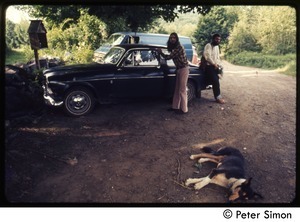 Two men by a parked Volvo, with a dog snoozing in the foreground, Tree Frog Farm commune