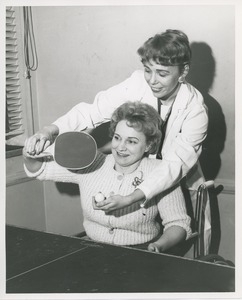 Mrs. Frances Marsala seated in her wheelchair playing ping pong assisted by attendant