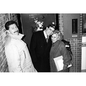 Two men and a woman in front of a door decorated with a picture of Santa Claus.