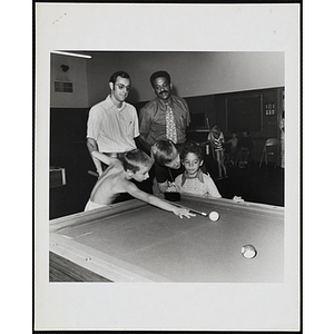 A Group of adults and children playing a game of pool