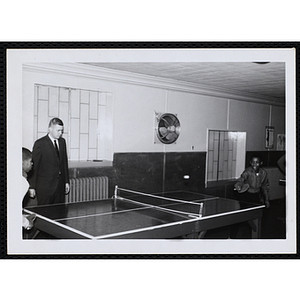 Two boys play table tennis as a man looks on