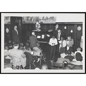 A man conducts three boys as they sing with piano accompaniment before an audience at a Christmas event