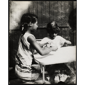 A girl and boy play cards at a table outdoors