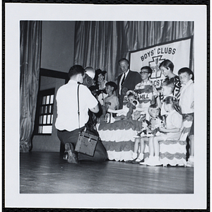 A photographer takes pictures of the Little Sister Contest winners posing with their brothers and three judges, including John W. Sears, at center