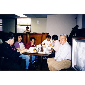 Four women and two men sit at a table, eating Thanksgiving dinner