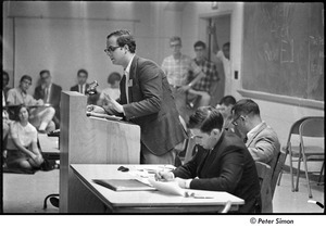 National Student Association Congress: man speaking at podium, Allard Lowenstein seated on right, wearing light suit