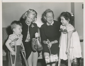 Margaret Milbank Bogert and an unidentified woman handing toys to two children on crutches