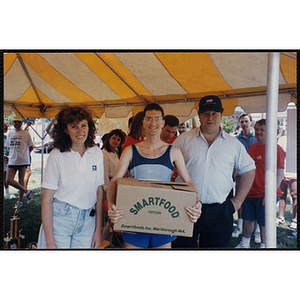 A runner holding a box poses with a woman and man during the Bunker Hill Road Race