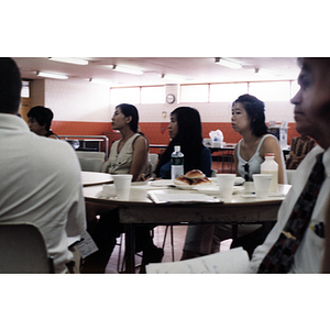 Three women sit at a table while listening to various speakers at a Chinese Resident Association celebration