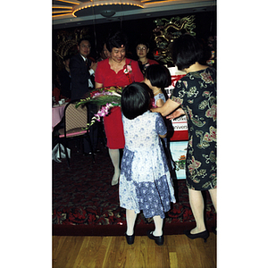 Two young girls present flowers to an award recipient at Chinese Progressive Association's 20th Anniversary Celebration
