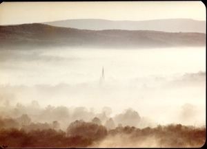 View of New England hills in the mist, a church steeple climbing through