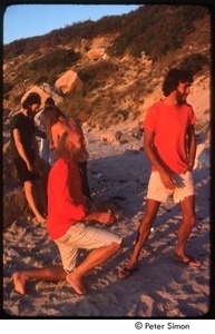 Ram Dass on his knees with an unidentified woman sitting on a rock at the beach