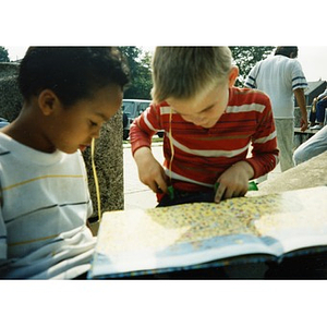 Two young boys look at a picture book, seated outside