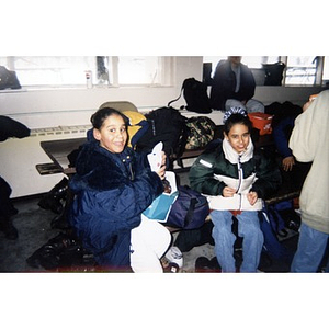Two girls on an Inquilinos Boricuas en Acción-sponsored ski trip inside the lodge with other participants and all their gear.