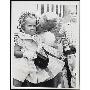 Miss South Boston, the winner of the Boys' Club Little Sister Contest, receives a kiss on the cheek from her brother who spreads her sash for the camera