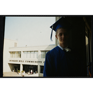 A teenage boy poses with the Bunker Hill Community College main entrance in the background during an Edwards School graduation ceremony