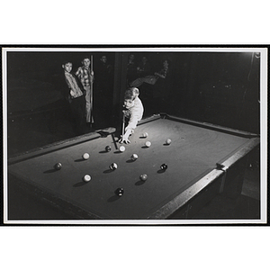 A Boy taking his turn in a pool game, while other boys look on in the background