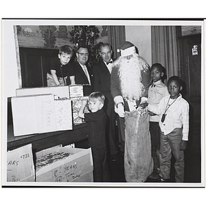 Santa Claus, boys and two men pose for a group shot with a bag of toys