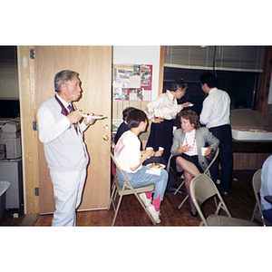 Six guests, seated and standing, eat and socialize at the victory party celebrating Dynasty Restaurant workers receiving their back wages