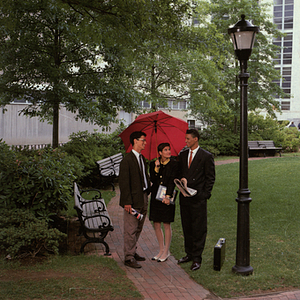 Three students under an umbrella on campus