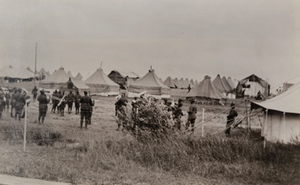 View of a black army band playing music amongst rows of tents in a German prisoners camp behind a barbed wire fence