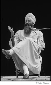 Yogi Bhajan seated onstage, talking to the audience at the Kohoutek Celebration of Consciousness