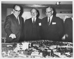 Dean Edward C. Moore with two unidentified men gesturing towards a scale model of the Umass campus