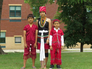 A photograph of Meh Mo posing with two boys in traditional Karenni clothing in Lowell, Massachusetts, 2014
