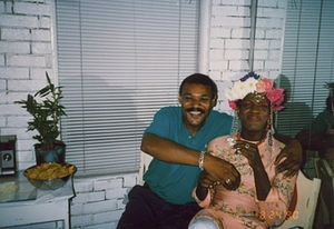 A Photograph of Marsha P. Johnson at Her Birthday Party, Sitting Next to a Friend Whose Arm is Wrapped Around Her