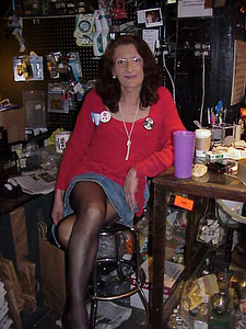 Photographs of Sylvia Rivera Sitting in a Red Shirt, Jean Skirt, and Black Tights with Her Legs Crossed