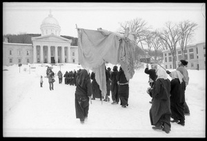 Protesters from Bread and Puppet Theater, dressed in cloaks and masks, unfurl a banner or puppet during a demonstration against the invasion of Laos at the Vermont State House