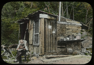 Old man reading outside of wooden hut