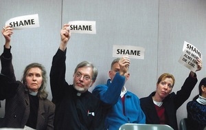 Protest by clergy members, holding up signs reading 'Shame,' relative to proposal on pay for non-union employees