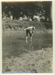 John S. Bailey outdoors, bending over while wading in water