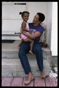 Johnnetta Cole seated on the front steps of a house, holding Zena Allen