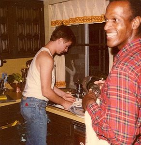 A Photograph of Marsha P. Johnson Wearing a Red Flannel Shirt While Washing the Dishes