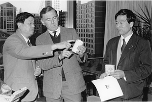 Mayor Raymond L. Flynn looking studying a cup with two unidentified men