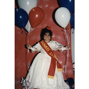 A little girl wears a Fantasía sash and holds balloons