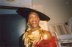 A Photograph of Marsha P. Johnson Wearing a Black Hat and a Gold Dress