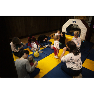 Young children seated with women on gym mats