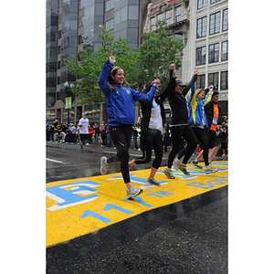 Five runners, holding hands with arms raised, cross the "One Run" finish line at Copley Square