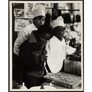 A boy divides cake in a pan as two other boys look on