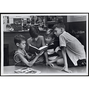 Four boys read a book at a table