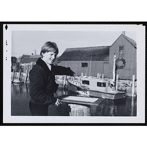 A boy stands on a dock and points at a boat