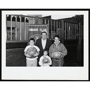 A woman, man and two children pose for a group shot with carved pumpkins in front of a Kiwanis Club banner